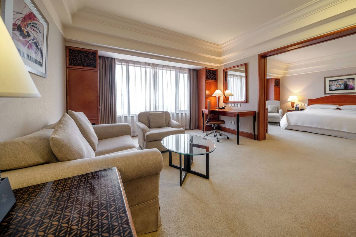 A hotel room with a sofa, armchair, desk, and a bed.