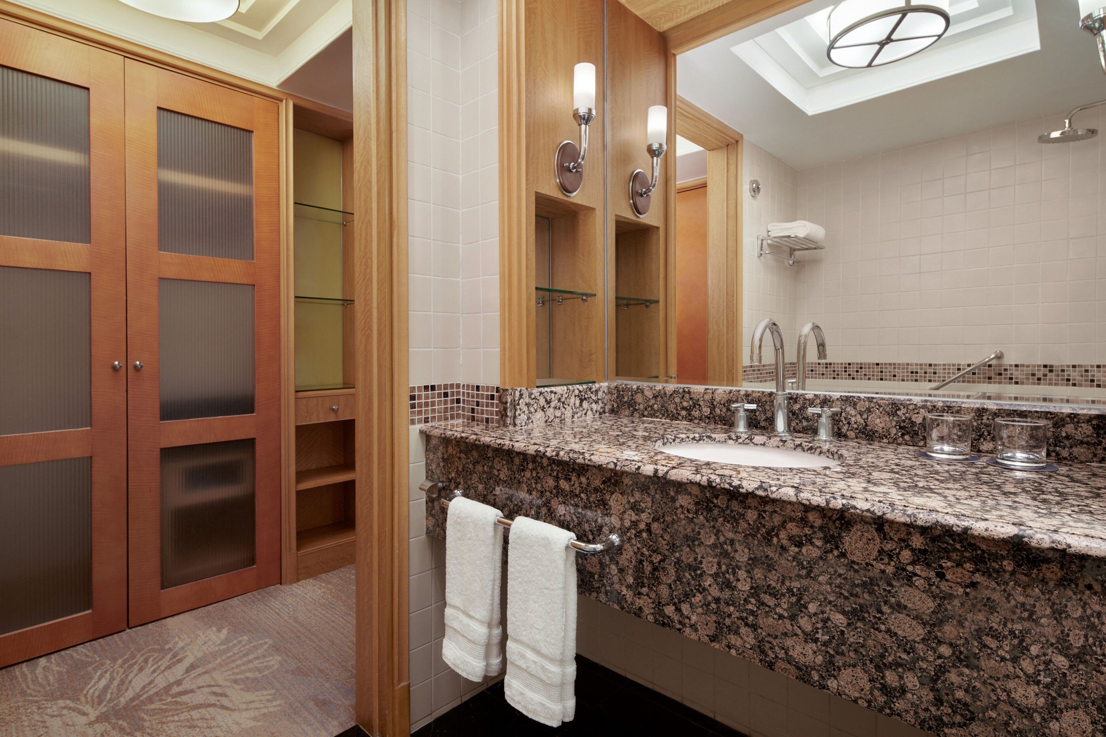 A bathroom with a granite countertop, a mirror, a towel rack, and a skylight.