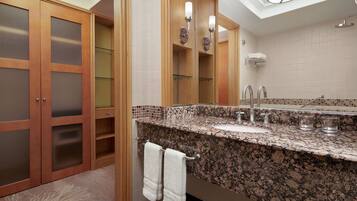 A bathroom with a granite countertop, a mirror, a towel rack, and a skylight.