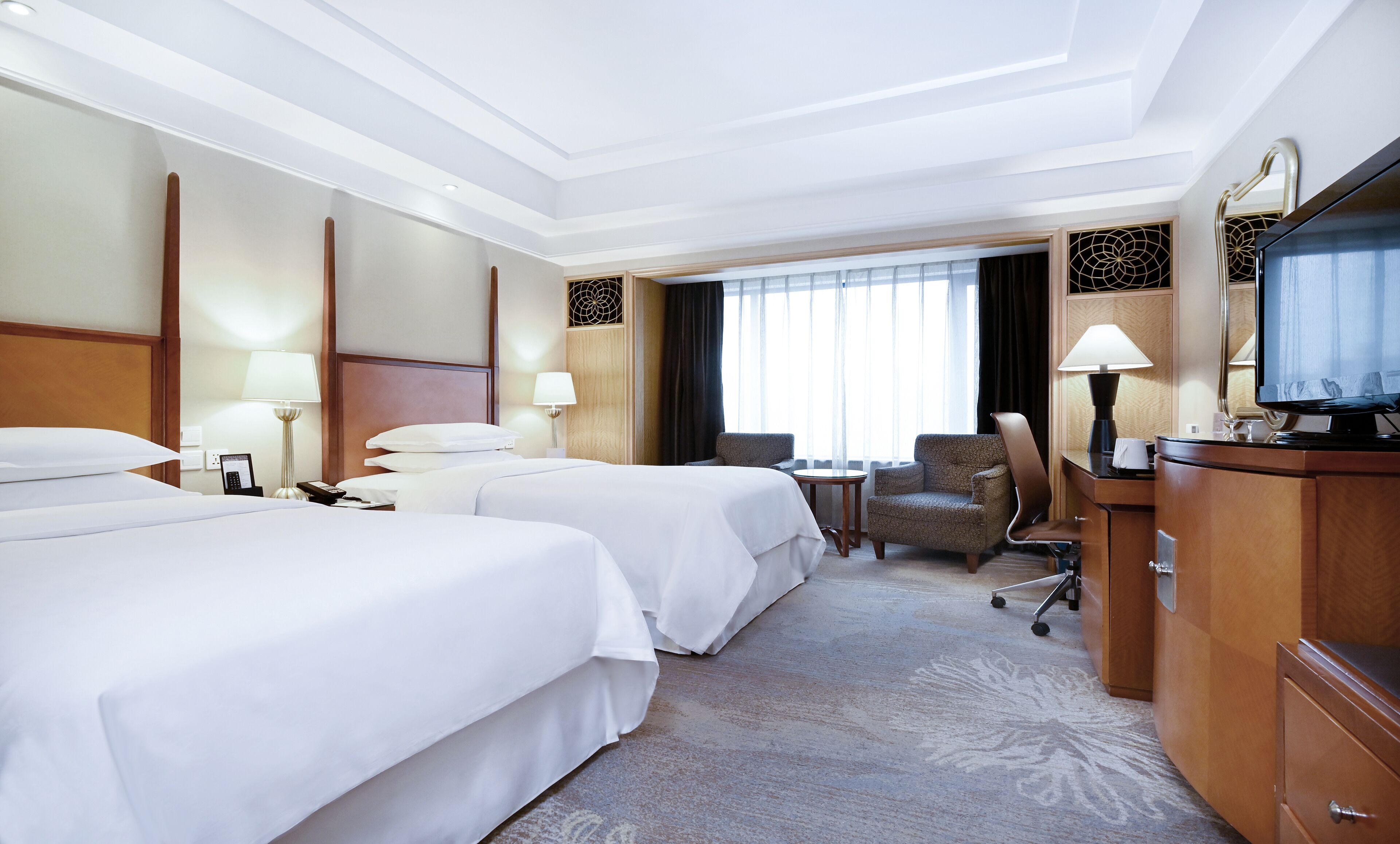 A hotel room with two beds, a desk with a chair, a television, and a window with curtains.