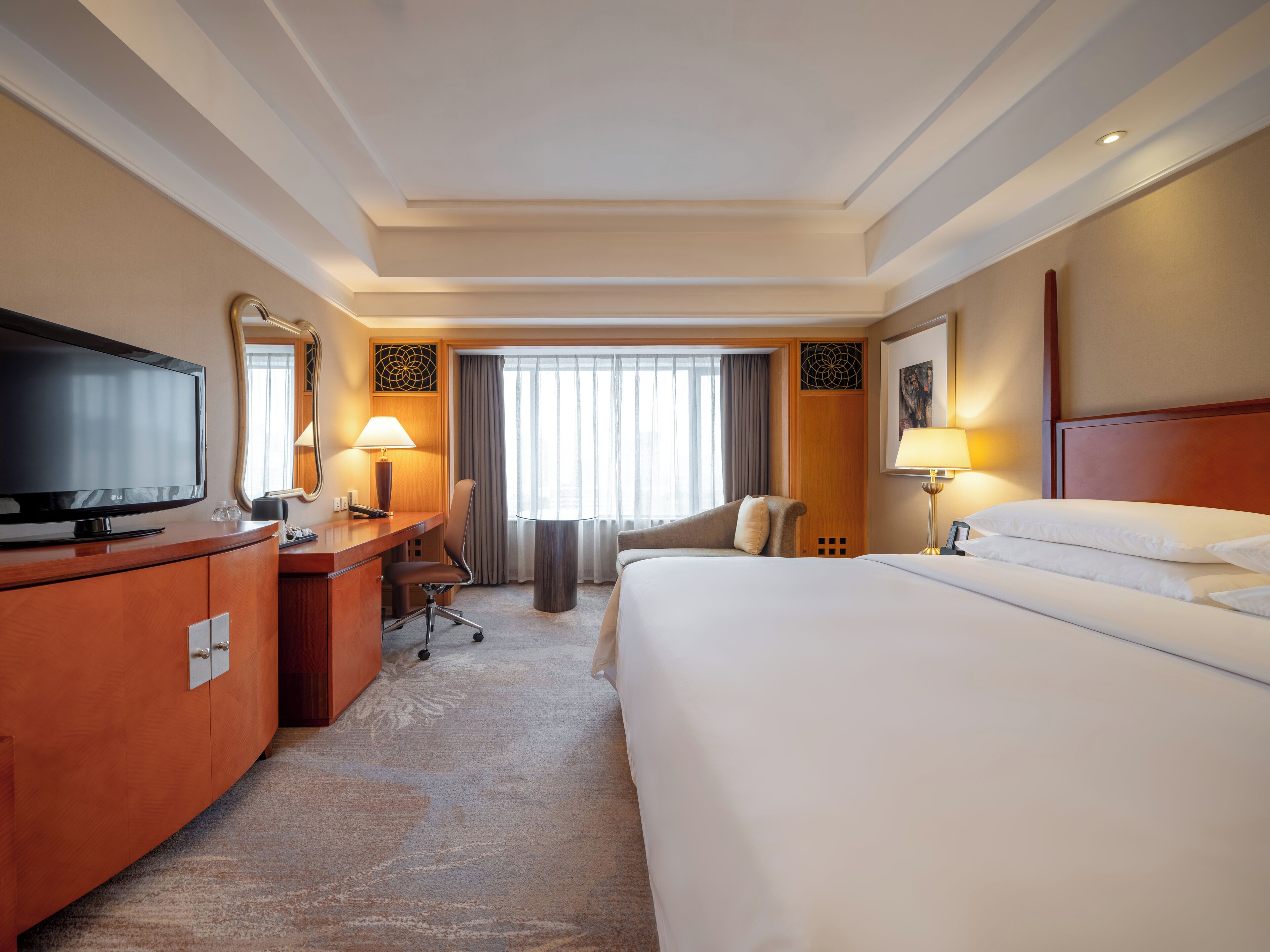 A hotel room with a large bed, a desk with a TV, a chair, and a lamp.