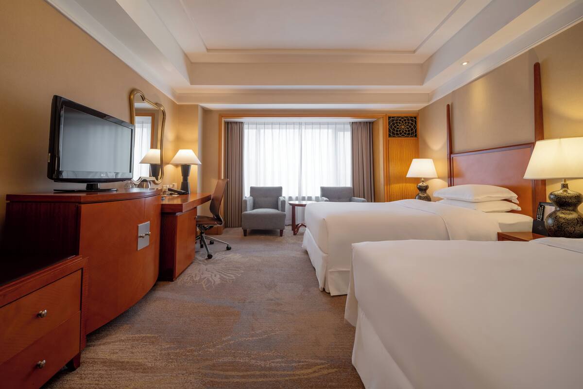 A hotel room with a television, two beds, a desk, and a chair.
