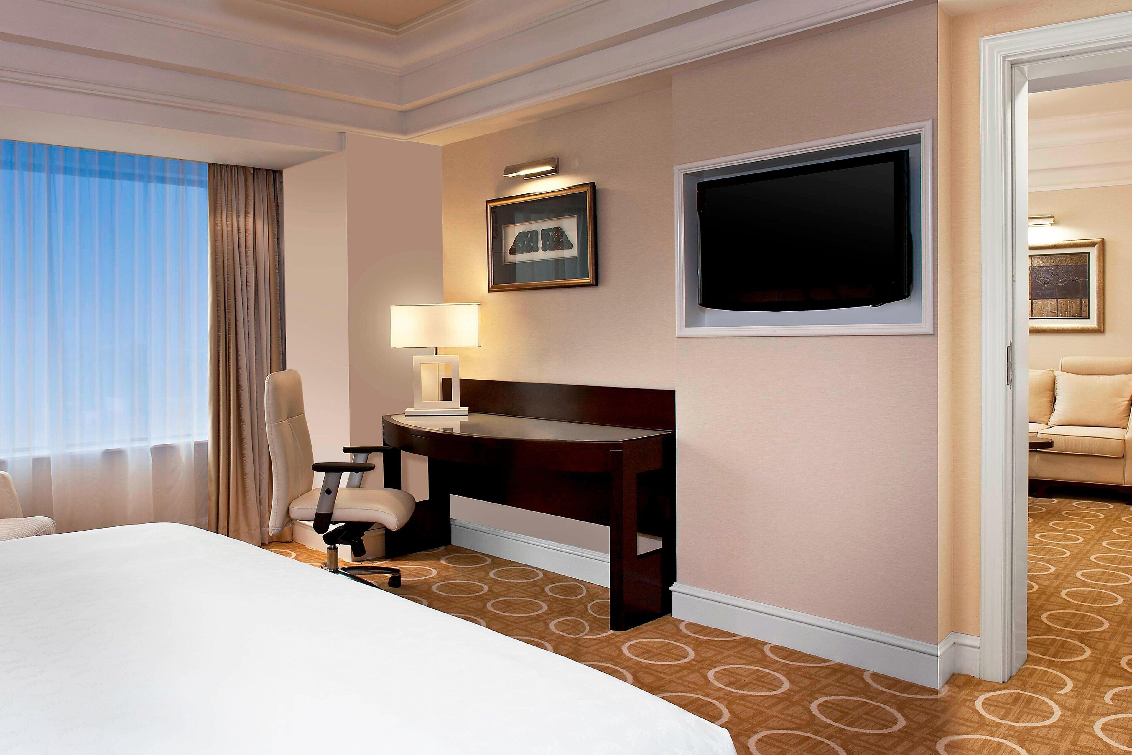 A hotel room with a bed, a desk with a chair, a television, and a painting on the wall.