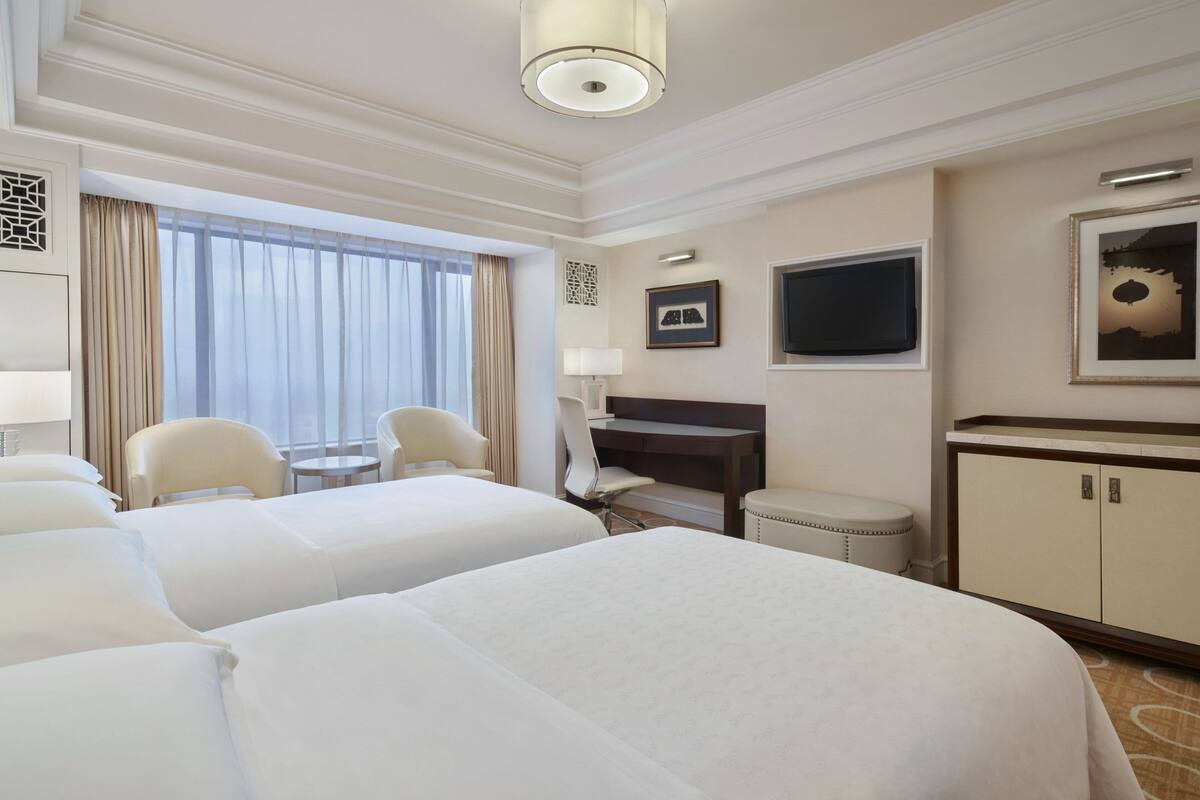 A hotel room with two beds, a desk, a chair, a TV, and a cabinet.