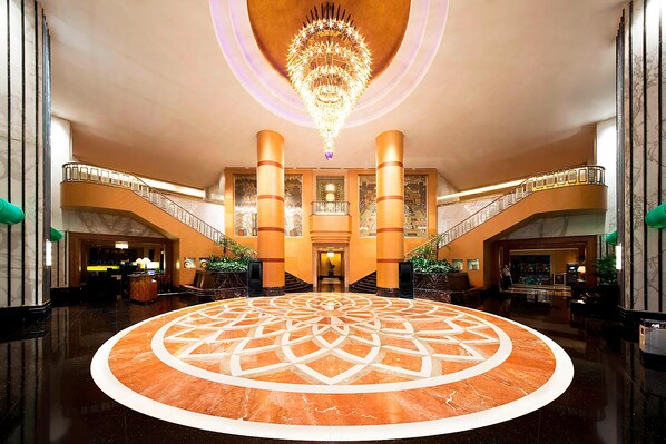 Un vaste hall d’entrée doté d’un motif circulaire au centre, d’un grand lustre et d’un escalier menant aux étages supérieurs.