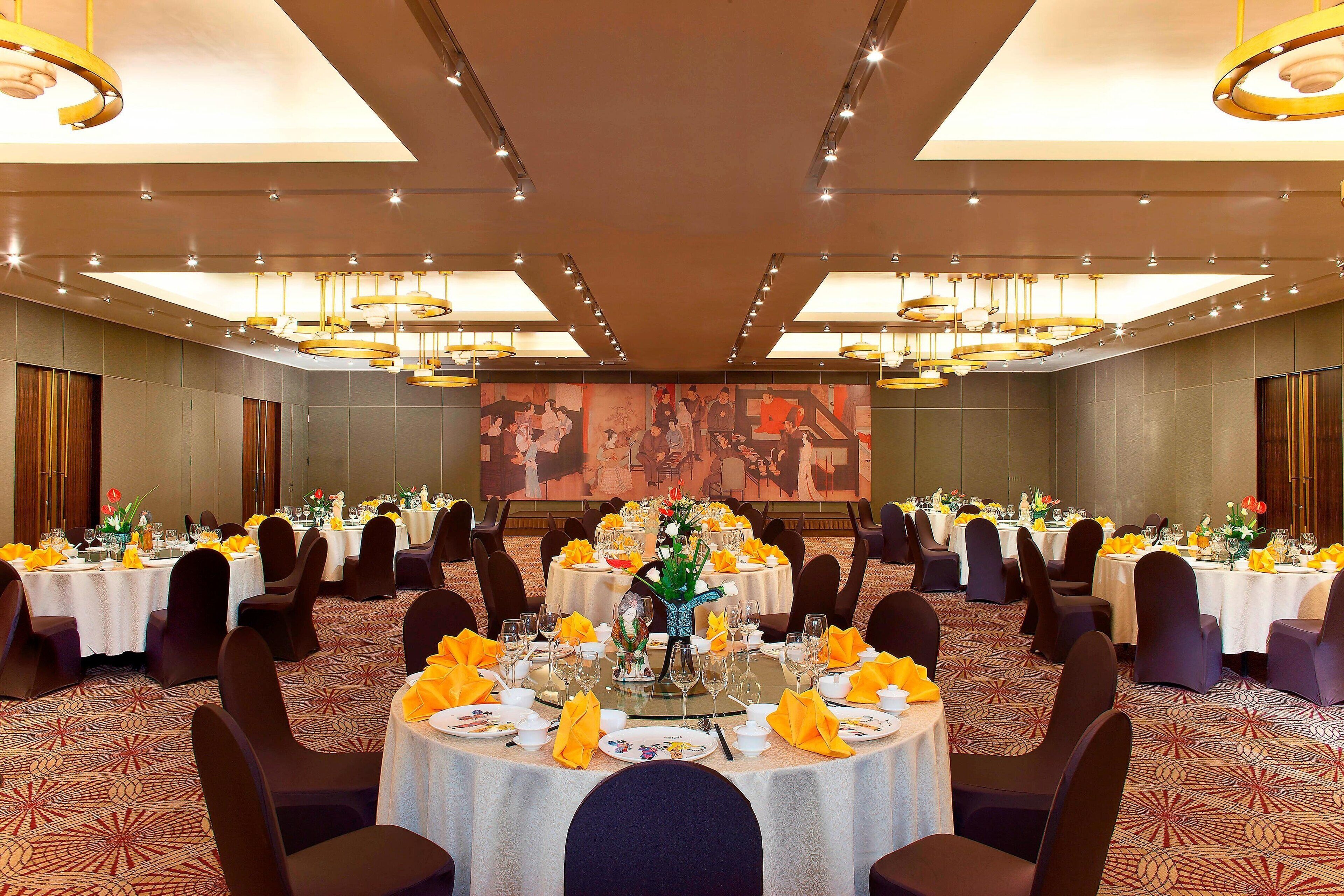A banquet hall with round tables set for dining, featuring yellow napkins and centerpieces.