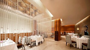 Un restaurante con varias mesas dispuestas para comer, con un diseño moderno, decoraciones colgantes y una paleta de colores cálidos.