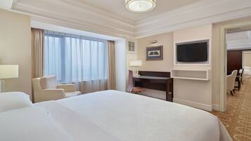 Une chambre d’hôtel avec un grand lit, un bureau, une télévision et un coin salon avec des fauteuils.