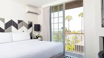 Habitación de hotel con cama, mesita de noche, lámpara, ventana con vista a palmeras y un balcón.