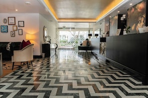 A hotel lobby with a herringbone floor pattern, a reception desk, and a seating area with a sofa and armchairs. - Chamberlain West Hollywood (West Hollywood)