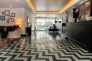 A hotel lobby with a herringbone floor pattern, a reception desk, and a seating area with a sofa and armchairs.