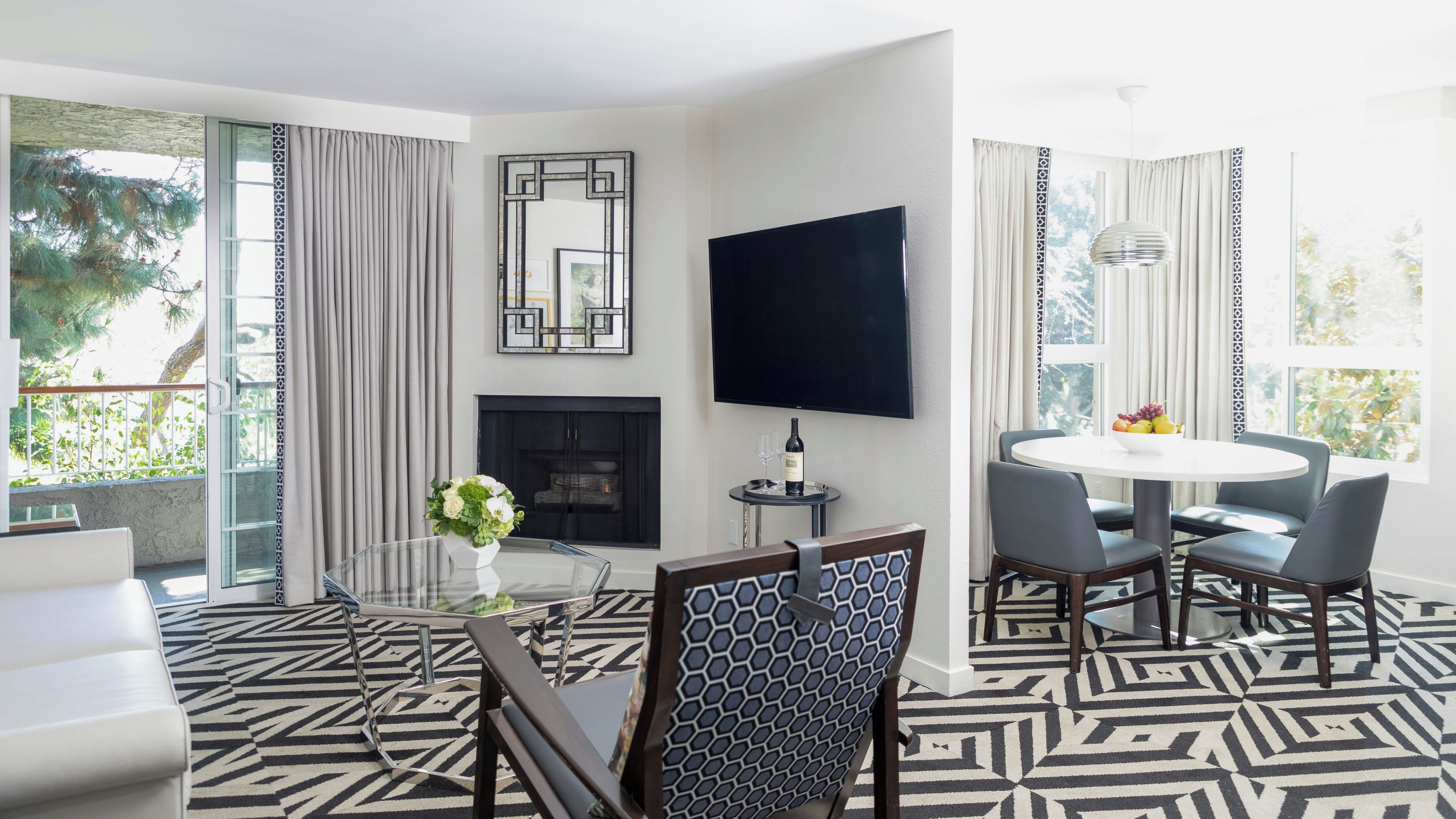 A modern living room with a fireplace, a flat-screen TV, a dining area with a round table, and a patterned floor.
