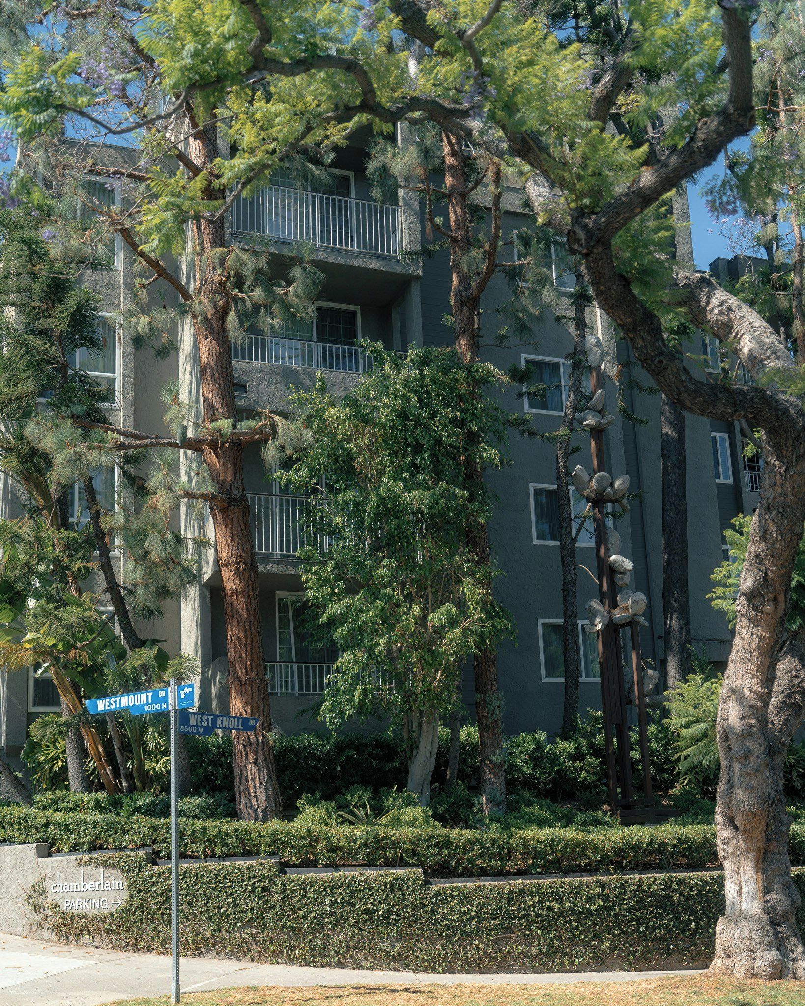 A multi-story residential building with balconies, surrounded by mature trees and a well-maintained garden.