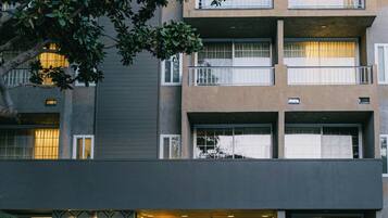 Un edificio de varios pisos con un diseño moderno, que cuenta con balcones, un acceso con diseño y un número de calle visible.