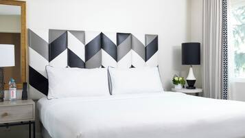 Une chambre d’hôtel comprenant un lit, une table de chevet, une lampe, un miroir et une œuvre d’art géométrique accrochée au mur.