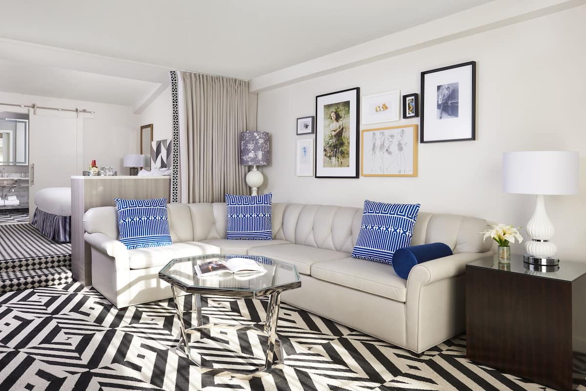 A modern living room with a sofa, coffee table, and a patterned rug. There is a bathroom visible in the background.
