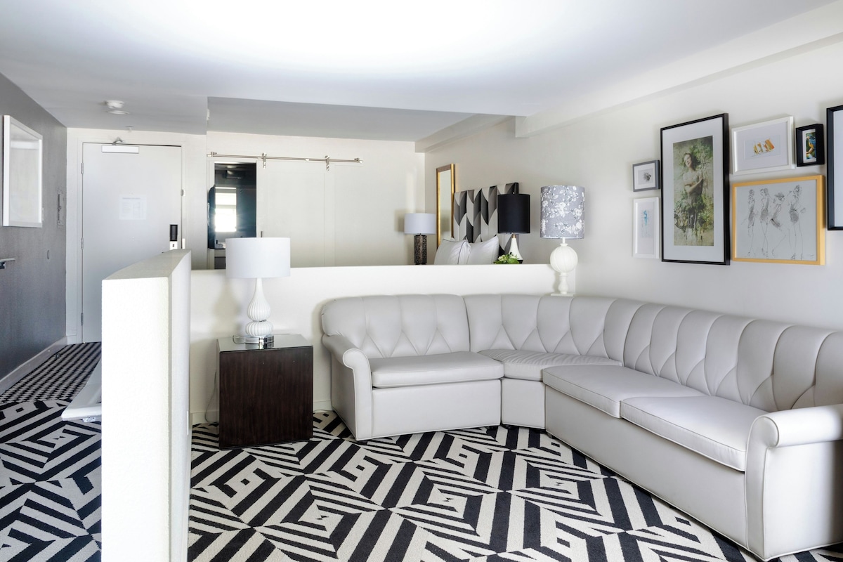 A modern living room with a white leather sofa, a patterned rug, and a wall with framed artwork.