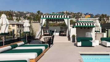 A rooftop pool area with lounge chairs, a covered seating area, and a view of the cityscape.