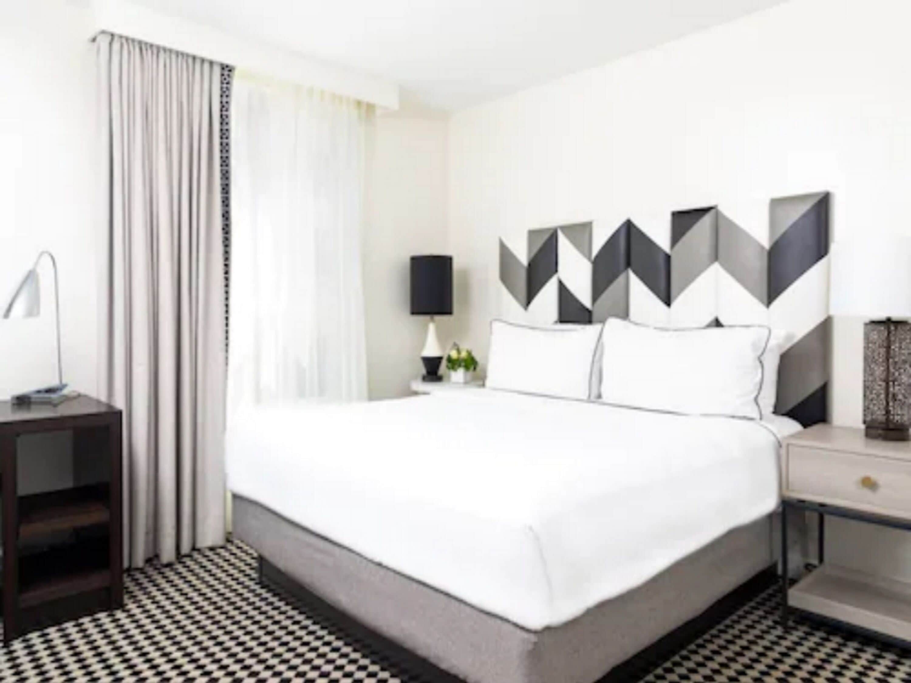 A hotel room with a bed, a nightstand, a lamp, and a geometric wall decoration.