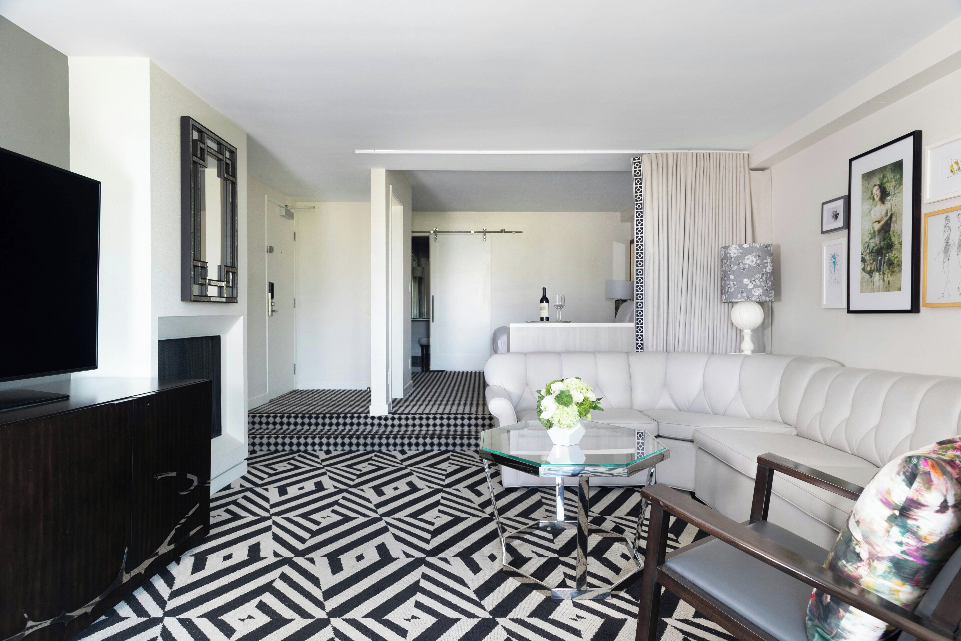 Uma sala de estar moderna com um chão estampado em preto e branco, um sofá branco, uma mesa de centro de vidro e uma televisão de tela plana.