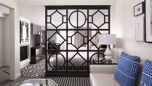 Una sala de estar moderna con piso de diseño geométrico, una pantalla decorativa blanco y negro, un sofá blanco con almohadones estampados en azul y una mesita de noche con una lámpara.