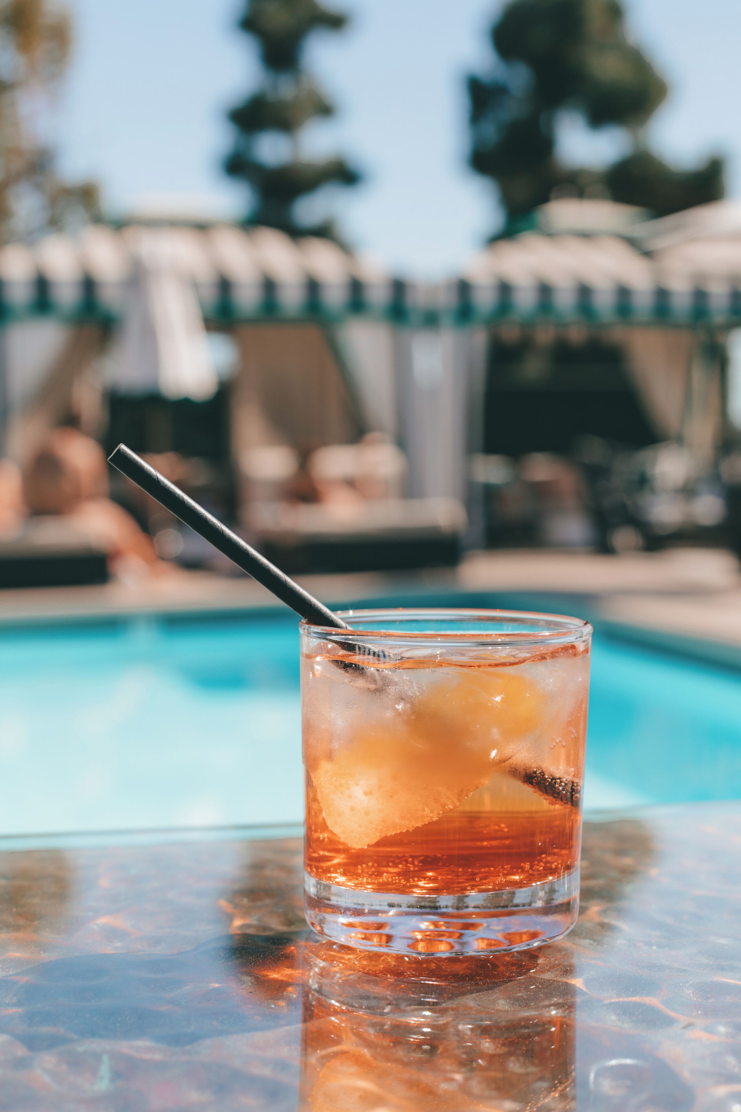 Ein Glas Eisgetränk mit Trinkhalm auf einem Tisch in Poolnähe.