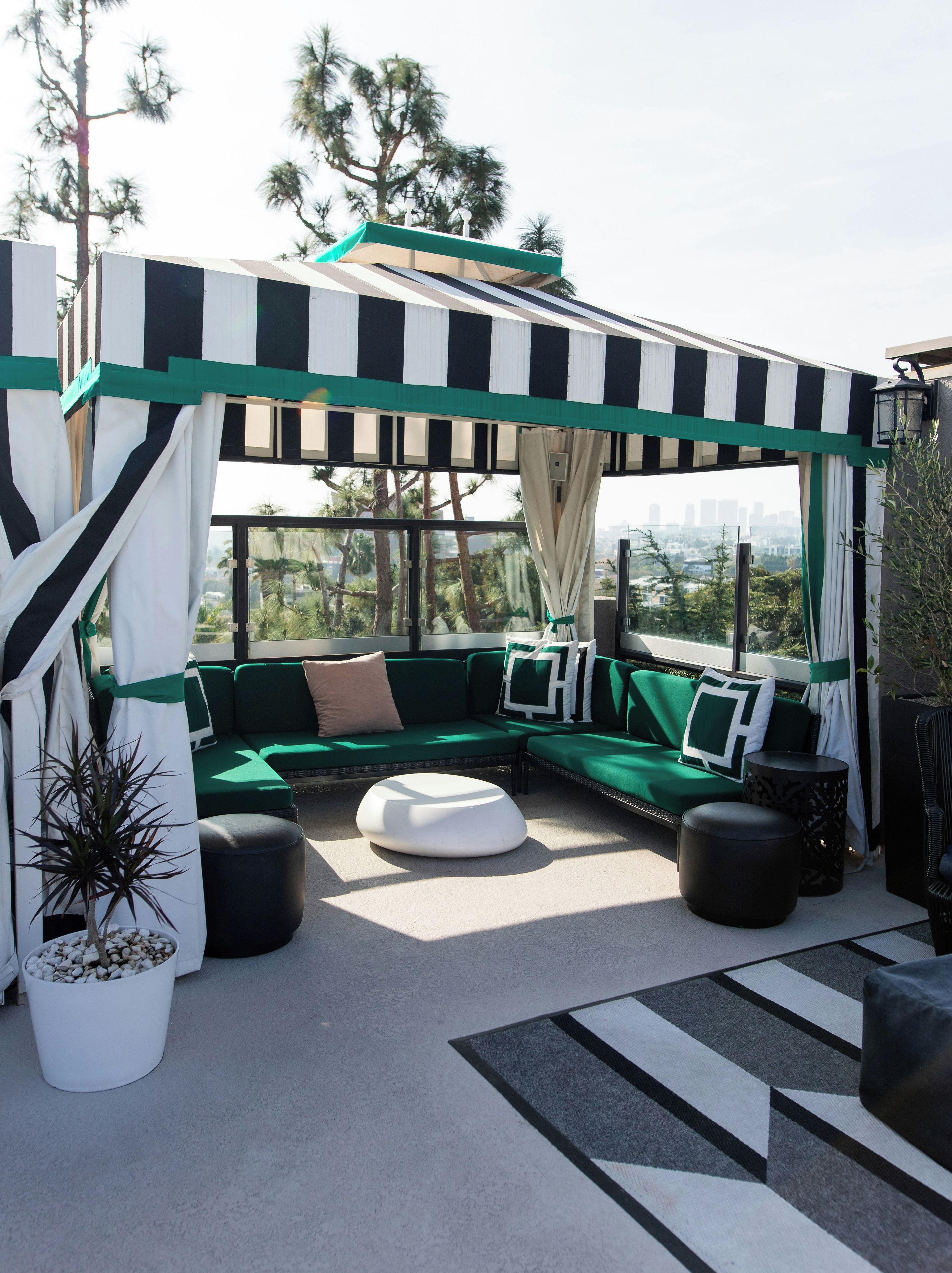 A covered outdoor seating area with a green sofa, white cushions, and a white ottoman.