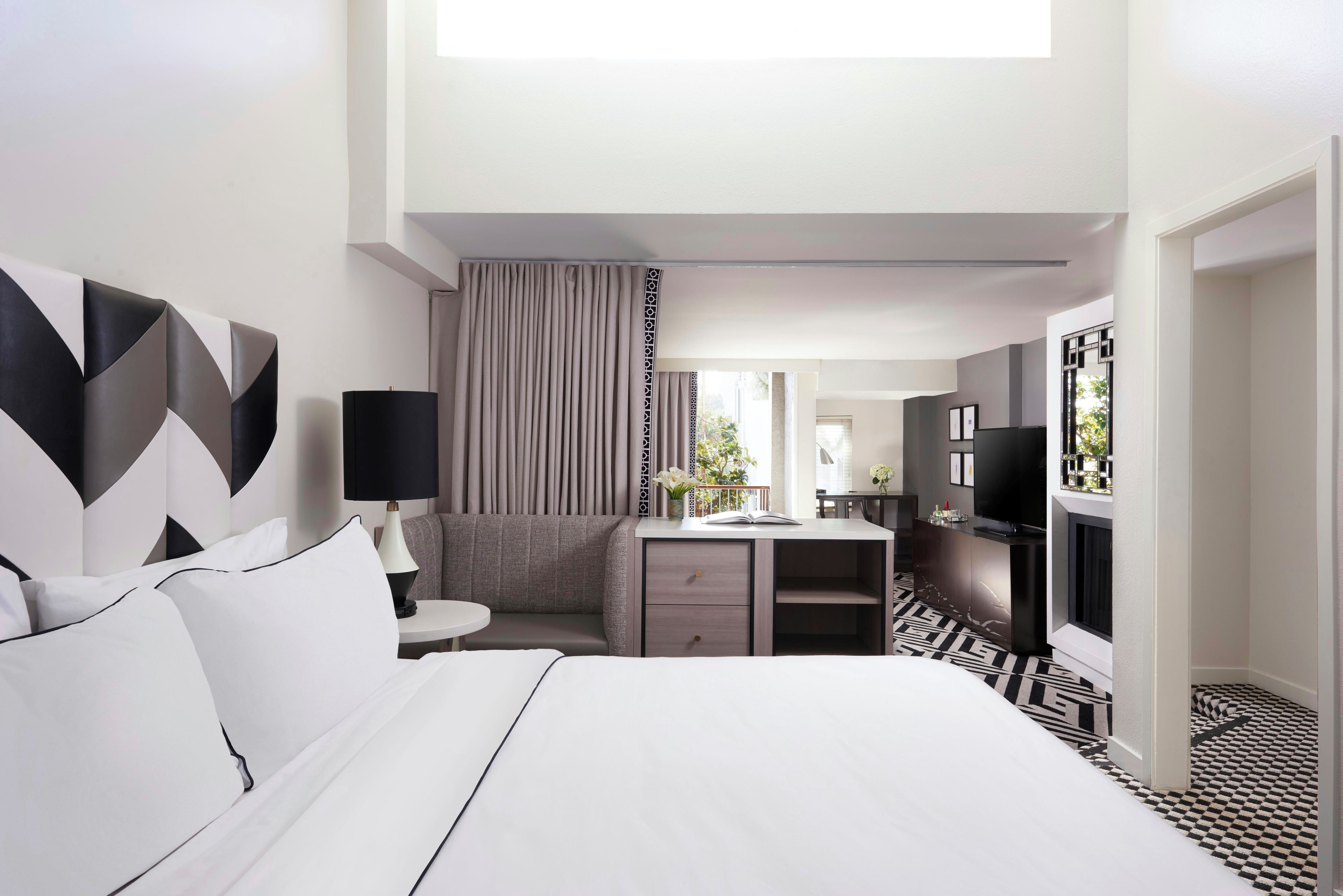 Ein Hotelzimmer mit Bett, Schreibtisch, Fernseher und einem durchgehenden Tür sichtbaren Badezimmer.