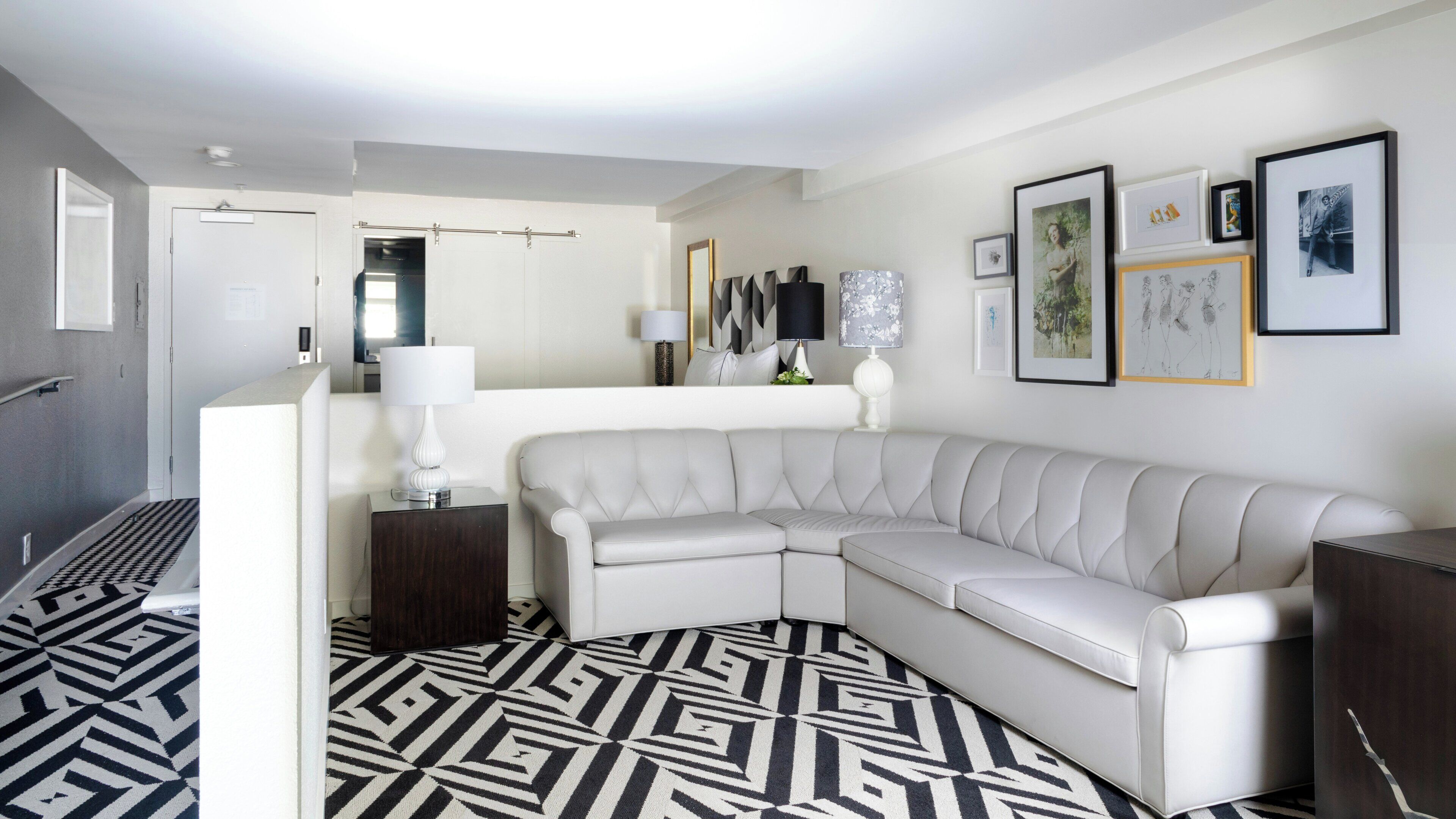 A modern living room with a white leather sofa, a patterned rug, and a wall with framed artwork.