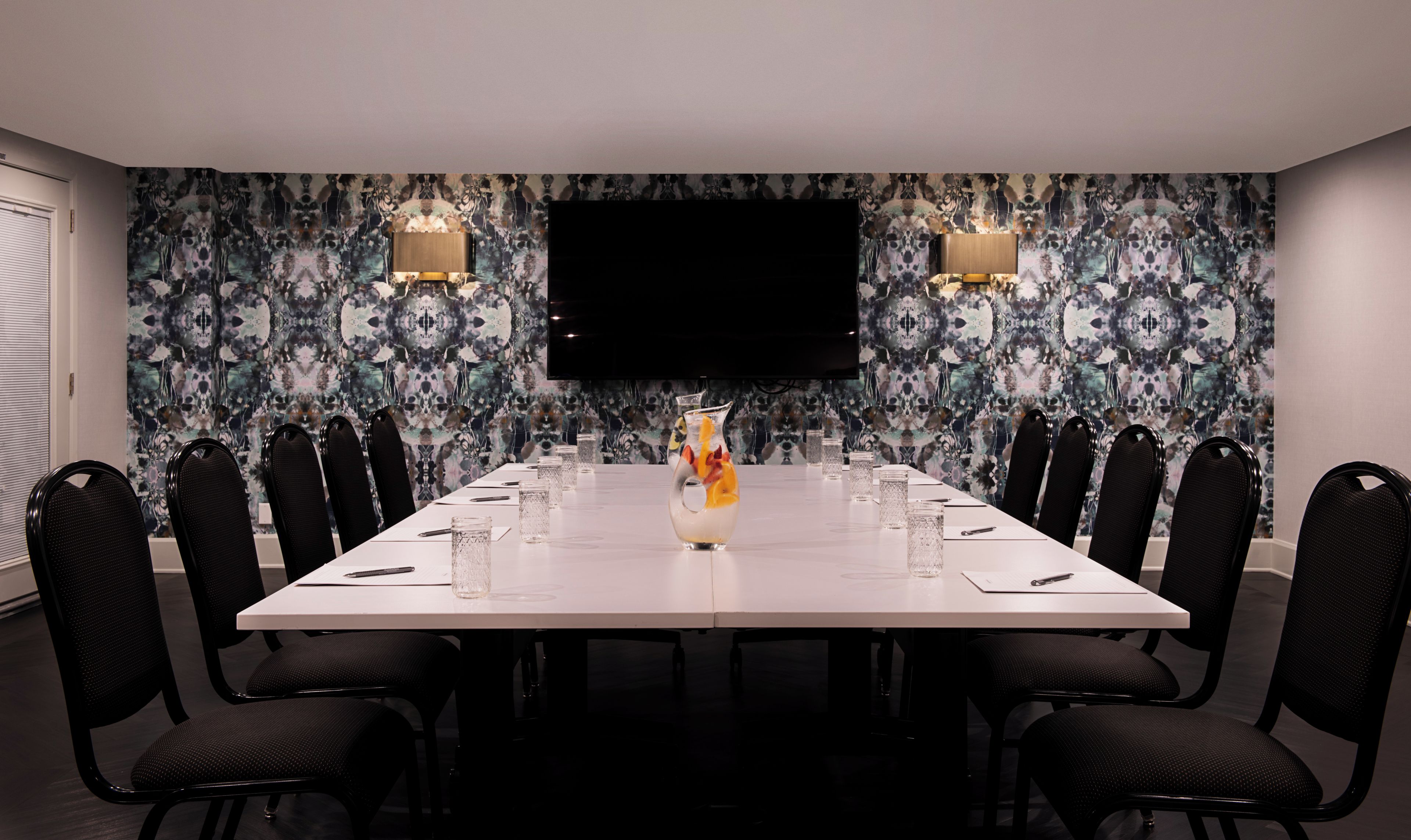 Une salle de conférence avec une longue table, des chaises, un vase décoratif et un téléviseur à écran plat fixé au mur.