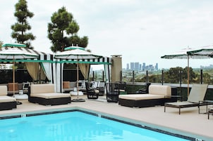 A rooftop pool area with lounge chairs and umbrellas, a city skyline view, and a pool with a clear blue color.