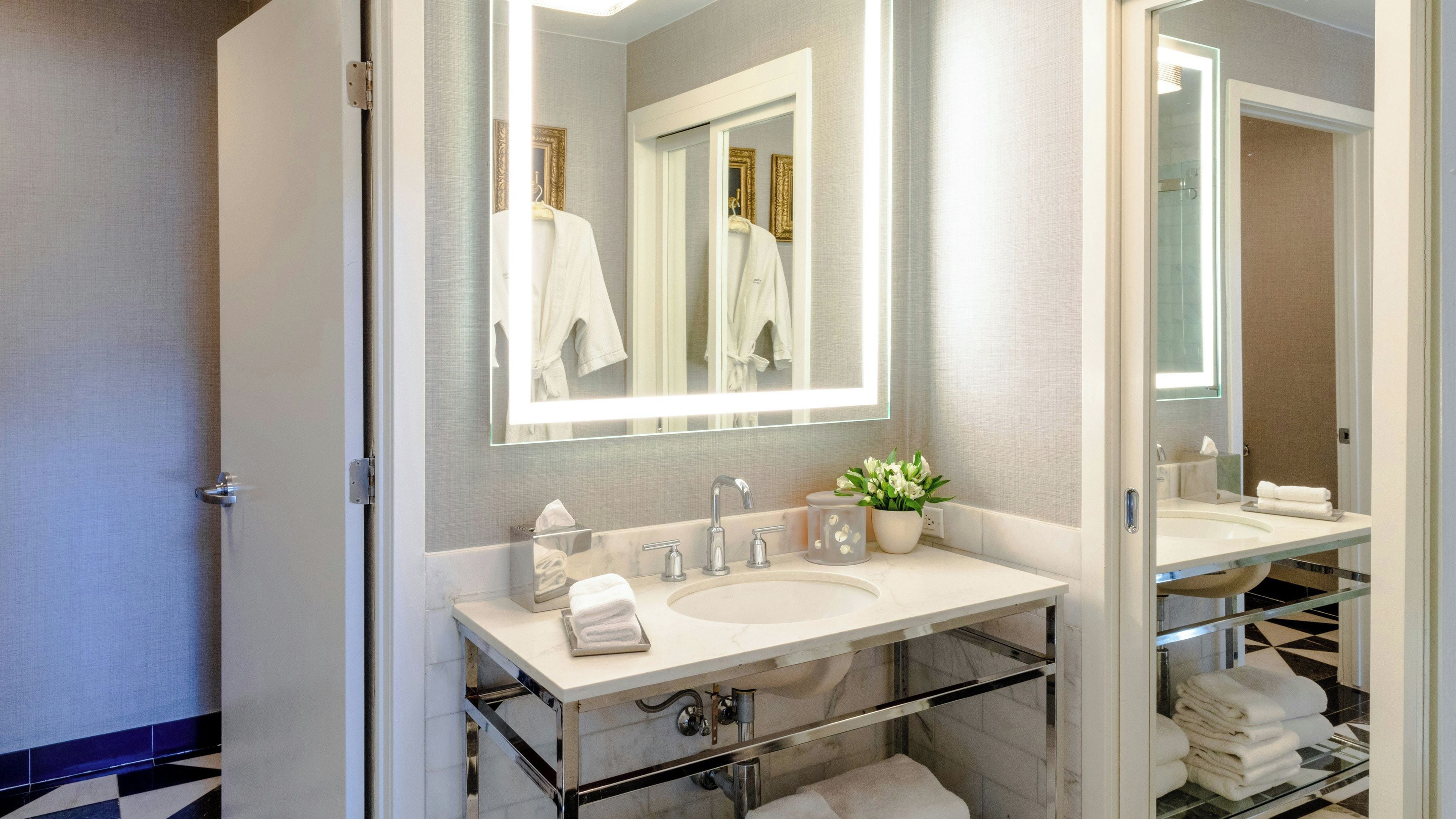 Une salle de bain moderne avec un grand miroir, deux vasques, une plante en pot et une cabine de douche en verre.