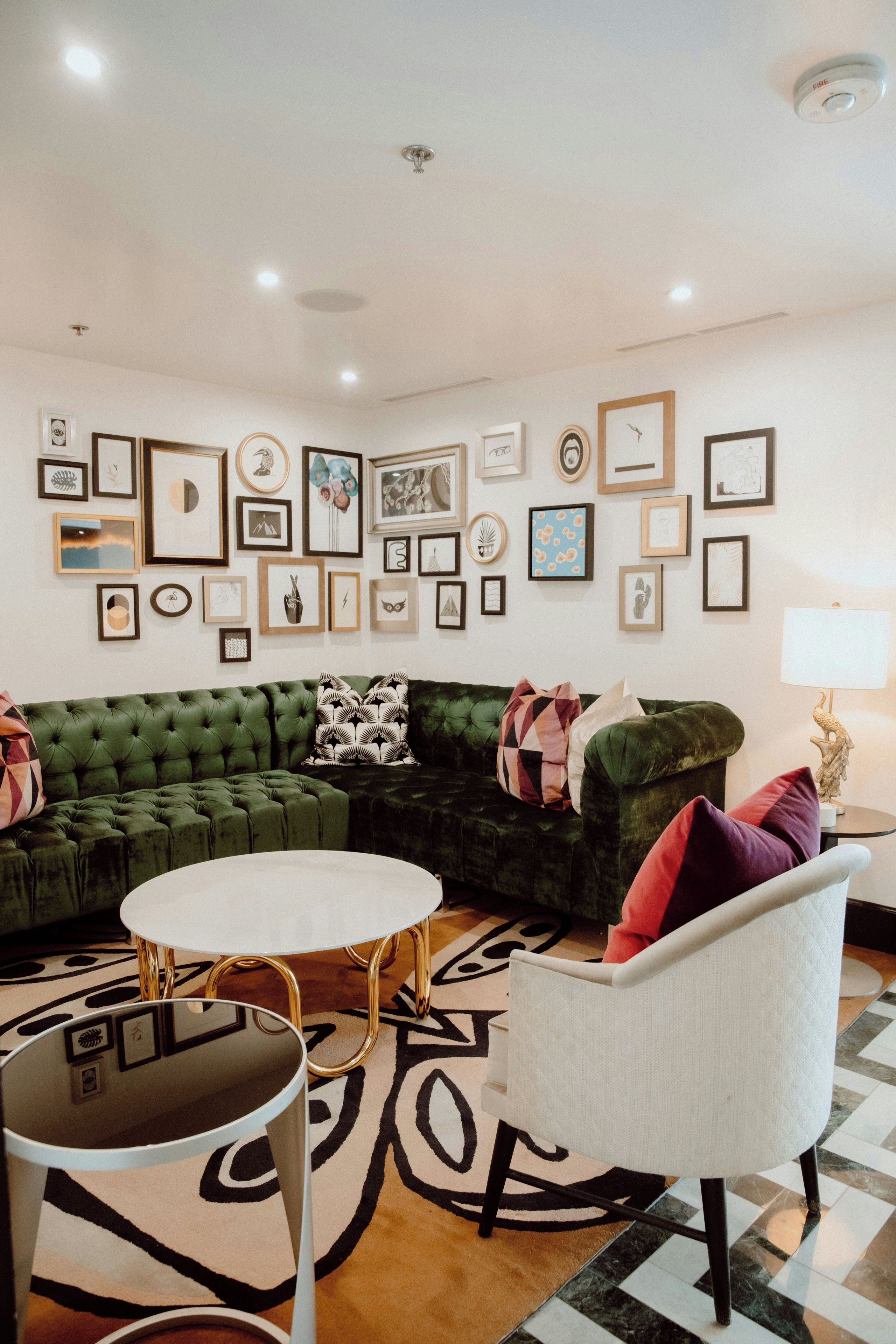 Een woonkamer met een groene bank, een witte fauteuil en een salontafel. Er hangen ingelijste foto's aan de muur.