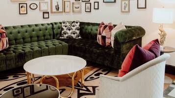 Een woonkamer met een groene bank, een witte fauteuil en een salontafel. Er hangen ingelijste foto's aan de muur.
