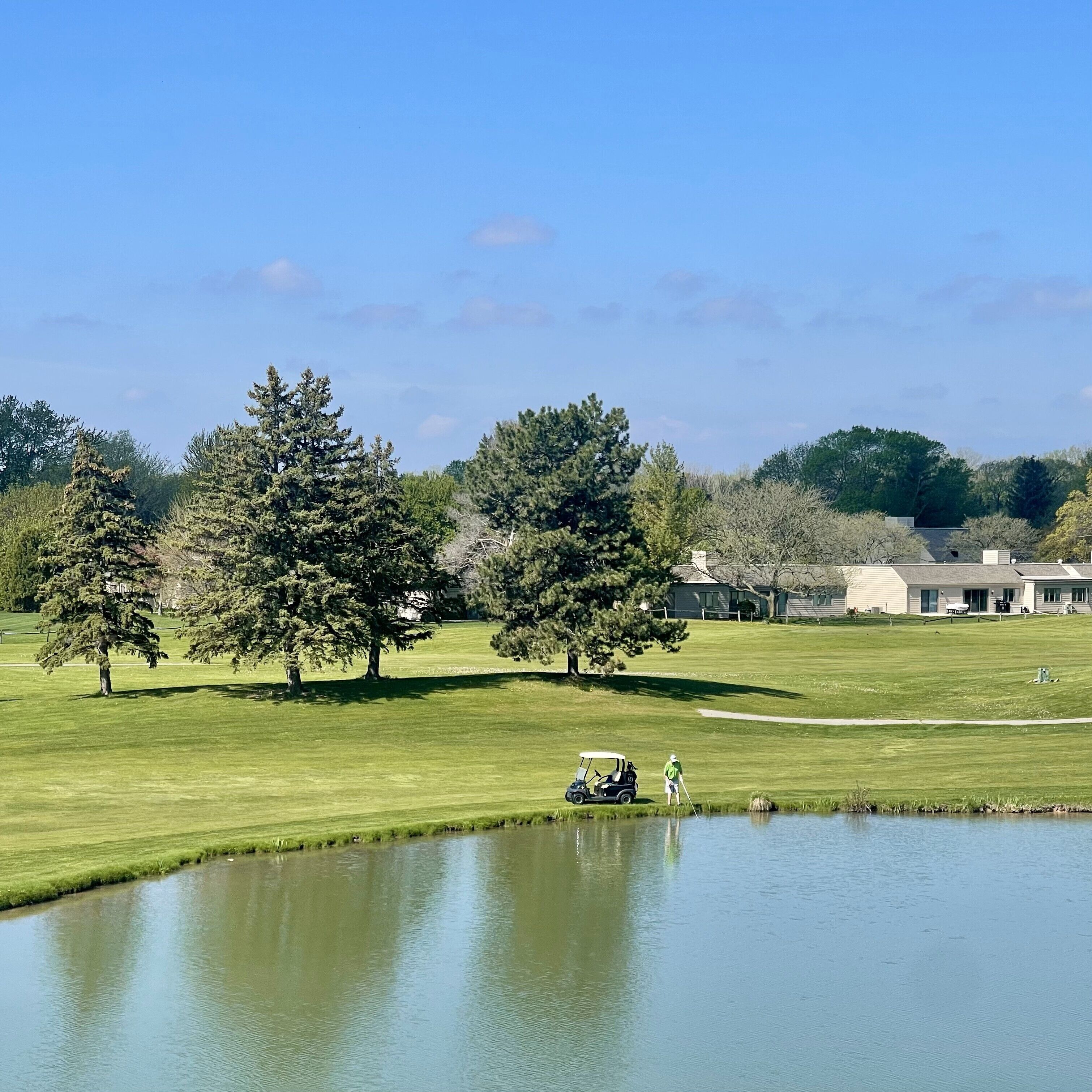 A golf course with a pond, trees, and a clubhouse in the background.