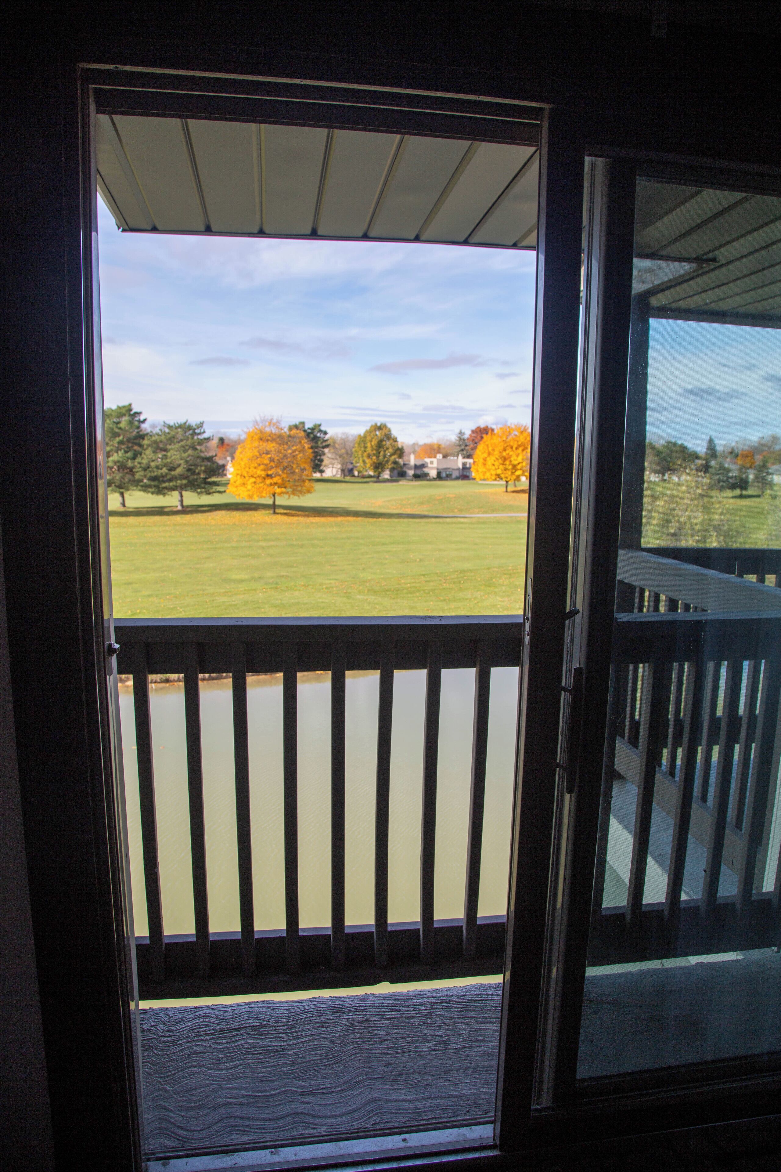 Une vue depuis un balcon doté d’une balustrade, donnant sur une zone herbeuse avec des arbres et un ciel dégagé.