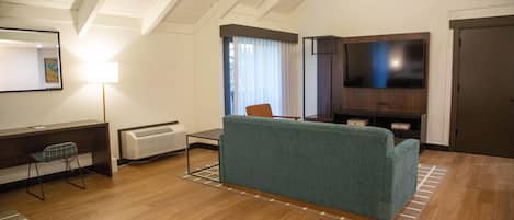 Una sala de estar con sofá, televisor, escritorio y silla, además de un radiador.