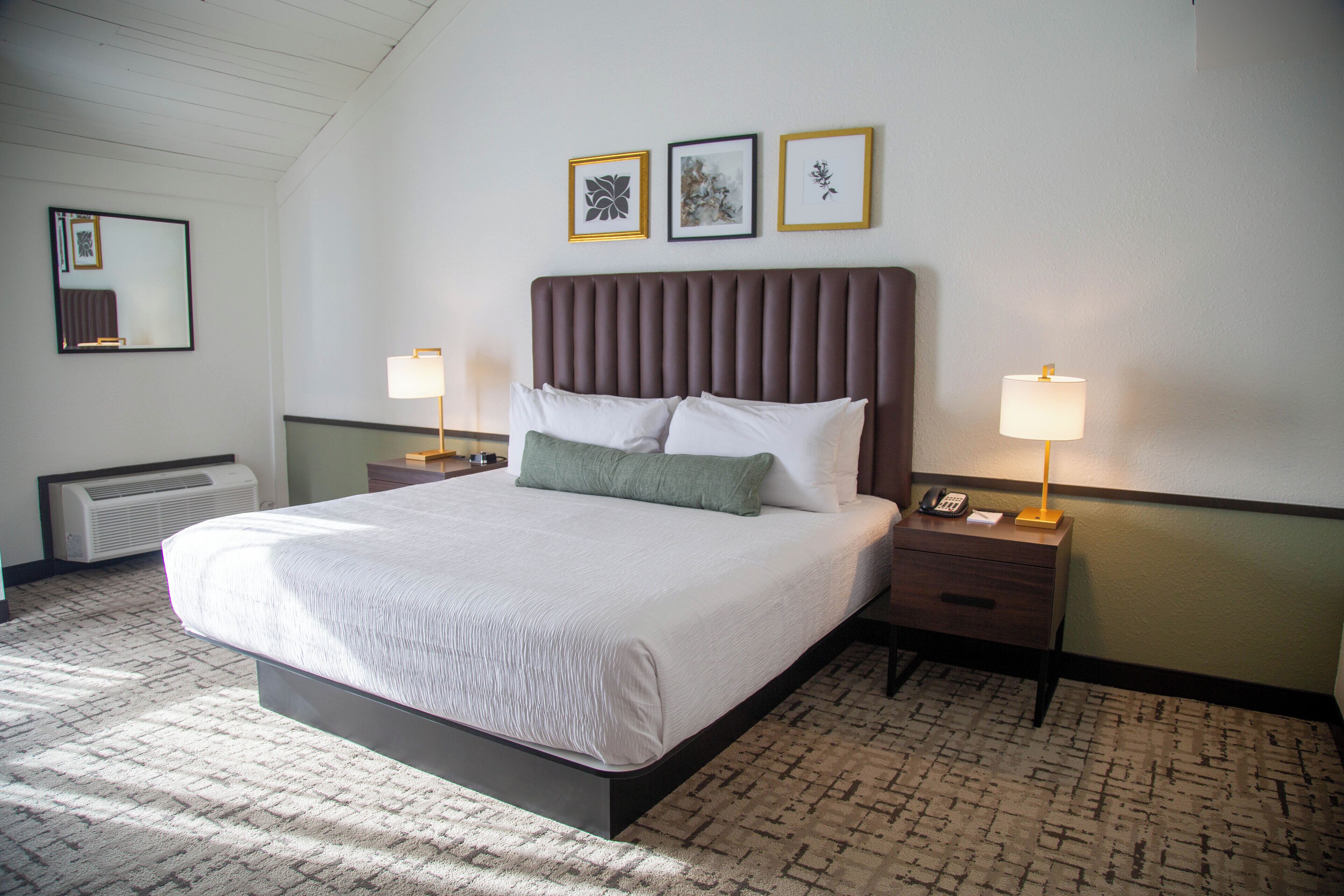 A neatly made bed with a headboard, two bedside tables with lamps, and three framed pictures on the wall.
