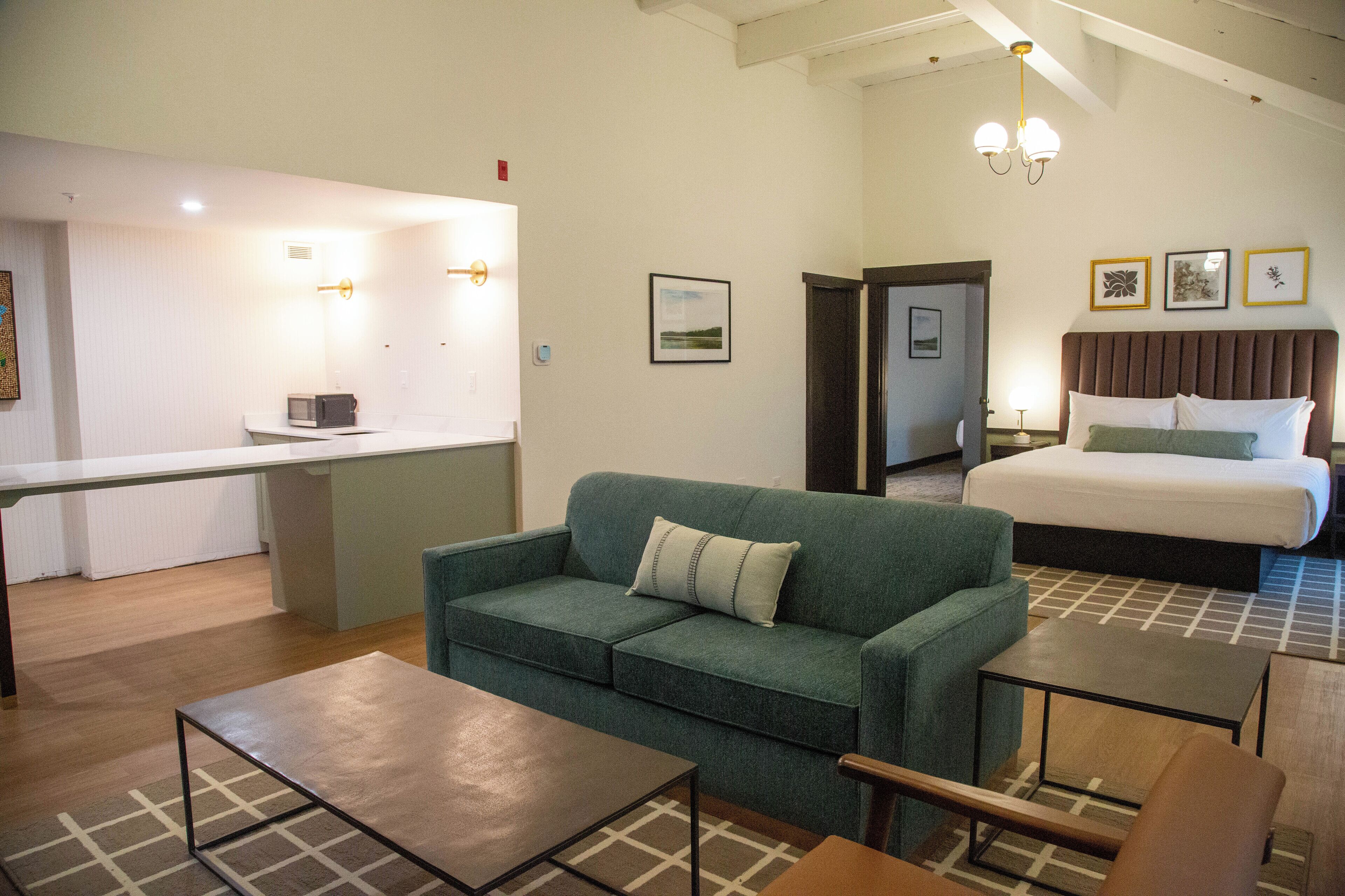Una habitación de hotel con una cama, un sofá verde, una mesita y una zona de kitchenette.