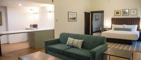 A hotel room with a bed, a green sofa, a small table, and a kitchenette area.