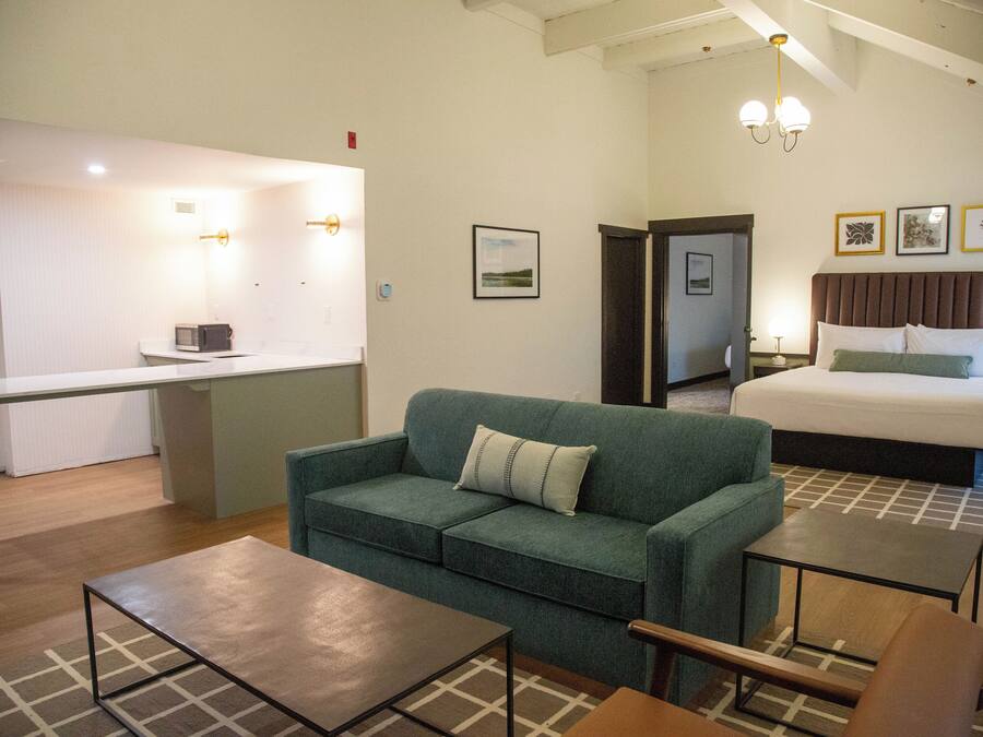 Una habitación de hotel con una cama, un sofá verde, una mesita y una zona de kitchenette.