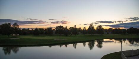 Un campo de golf tranquilo al anochecer, con un lago sereno que refleja el cielo y los árboles.
