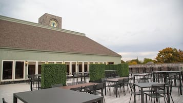 An outdoor patio with tables and chairs, a stone wall, and a building with a 'BV' logo.