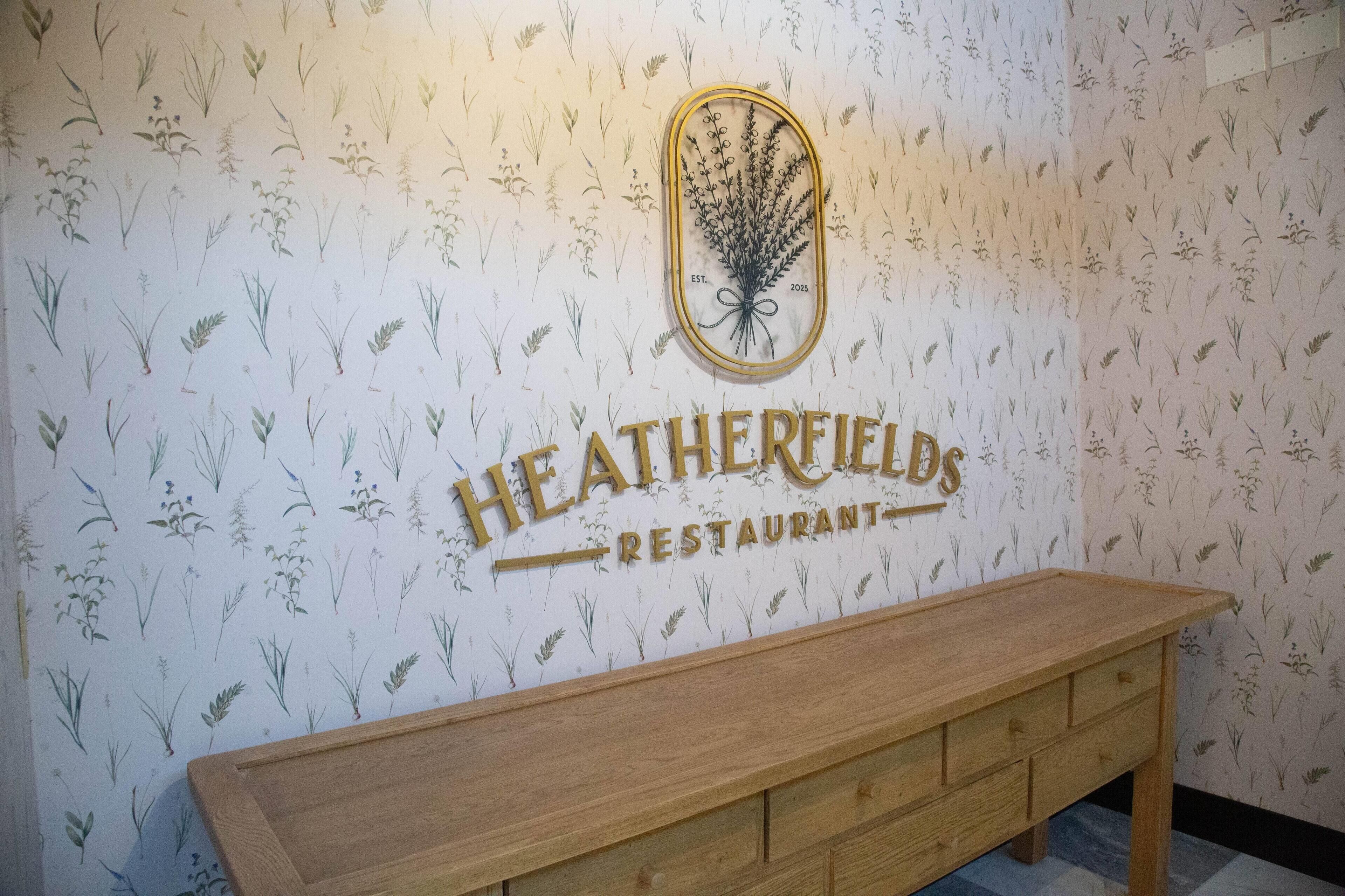 Eine Wand mit einem floralen Muster und der Schriftzug "HEATHERFIELDS RESTAURANT" gut sichtbar.