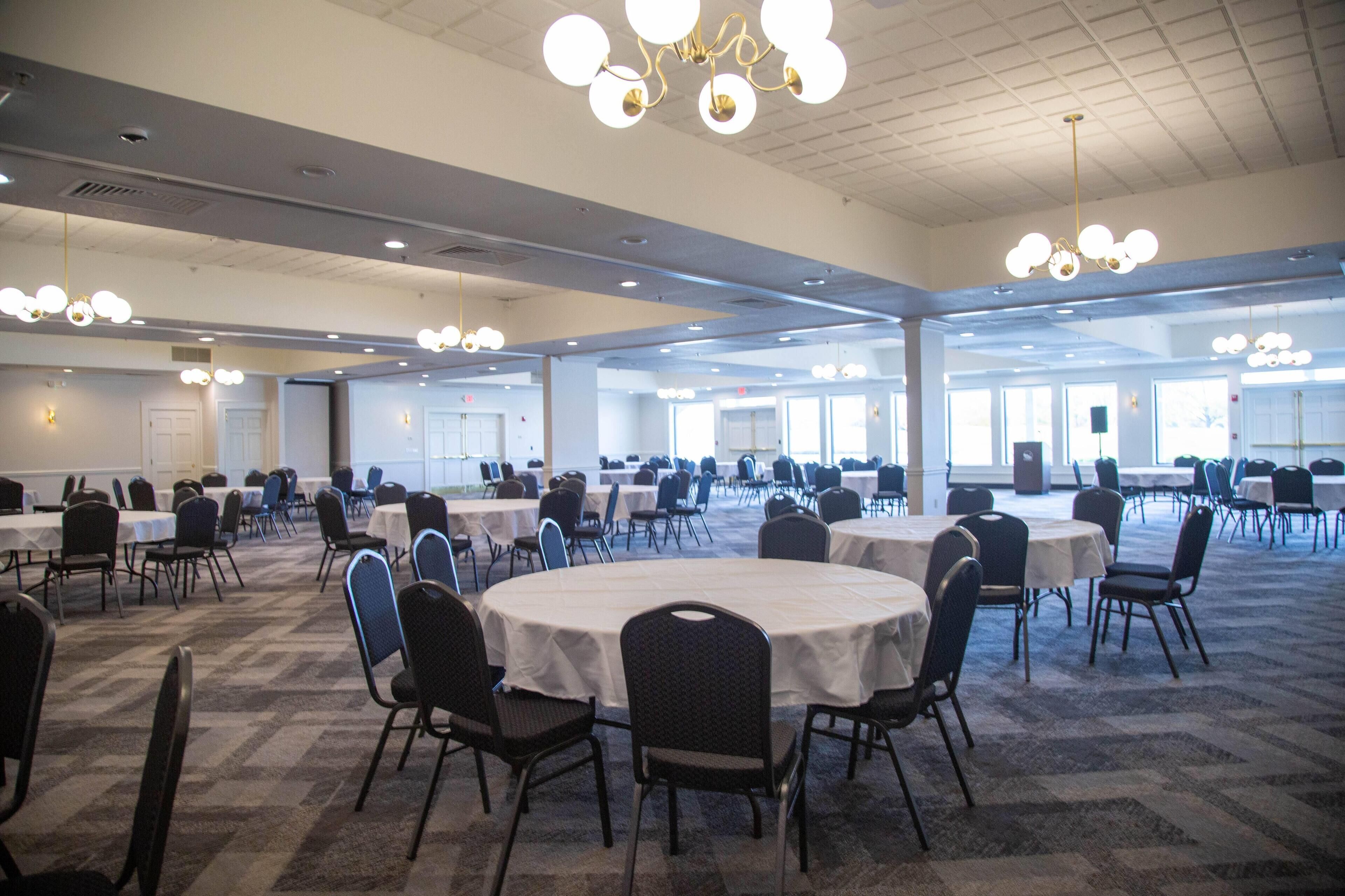 A large conference room with multiple round tables and chairs, arranged in rows.