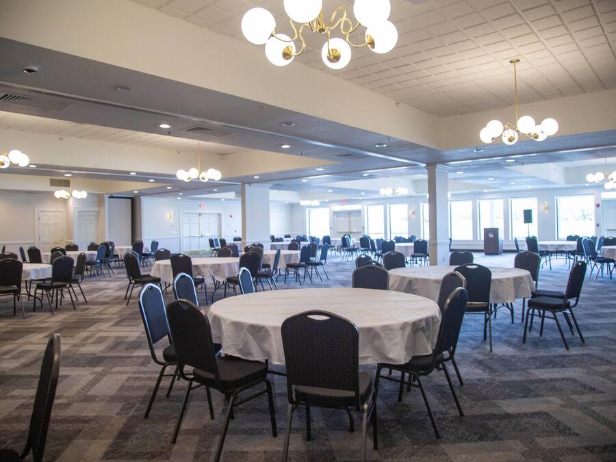 A large conference room with multiple round tables and chairs, arranged in rows.