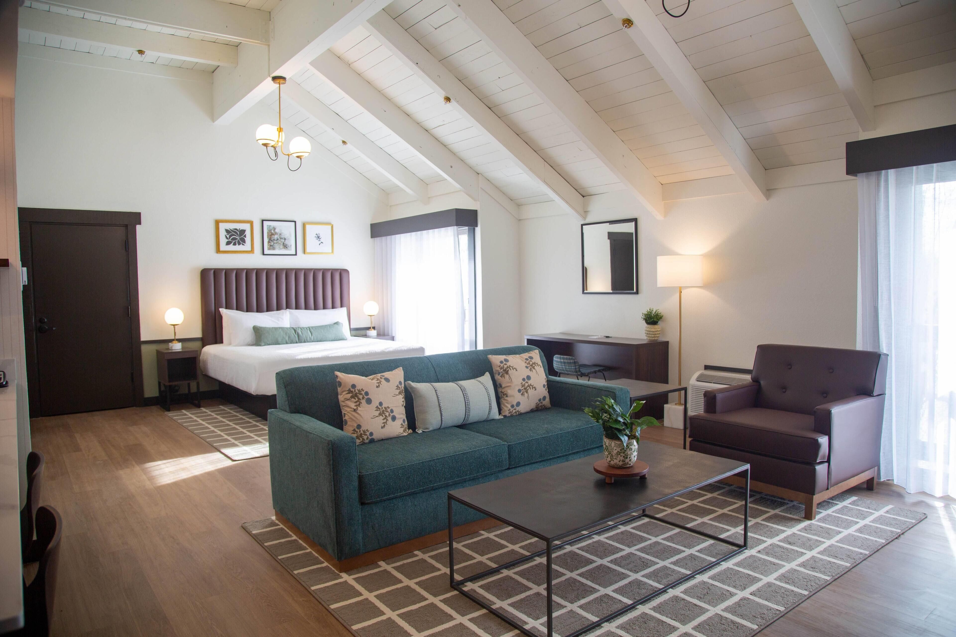 A modern hotel room with a bed, a sofa, a coffee table, and a desk.
