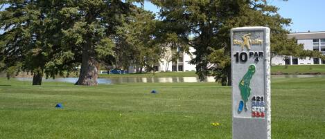 Un parcours de golf avec un panneau indiquant un trou à 10 coups, entouré d’arbres et avec un bâtiment visible au loin.