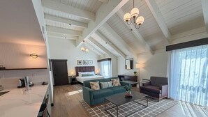 Une chambre d’hôtel moderne dotée d’une cuisine, d’un espace de vie avec un canapé et une table basse, d’un coin repas séparé et d’une grande fenêtre avec des rideaux.