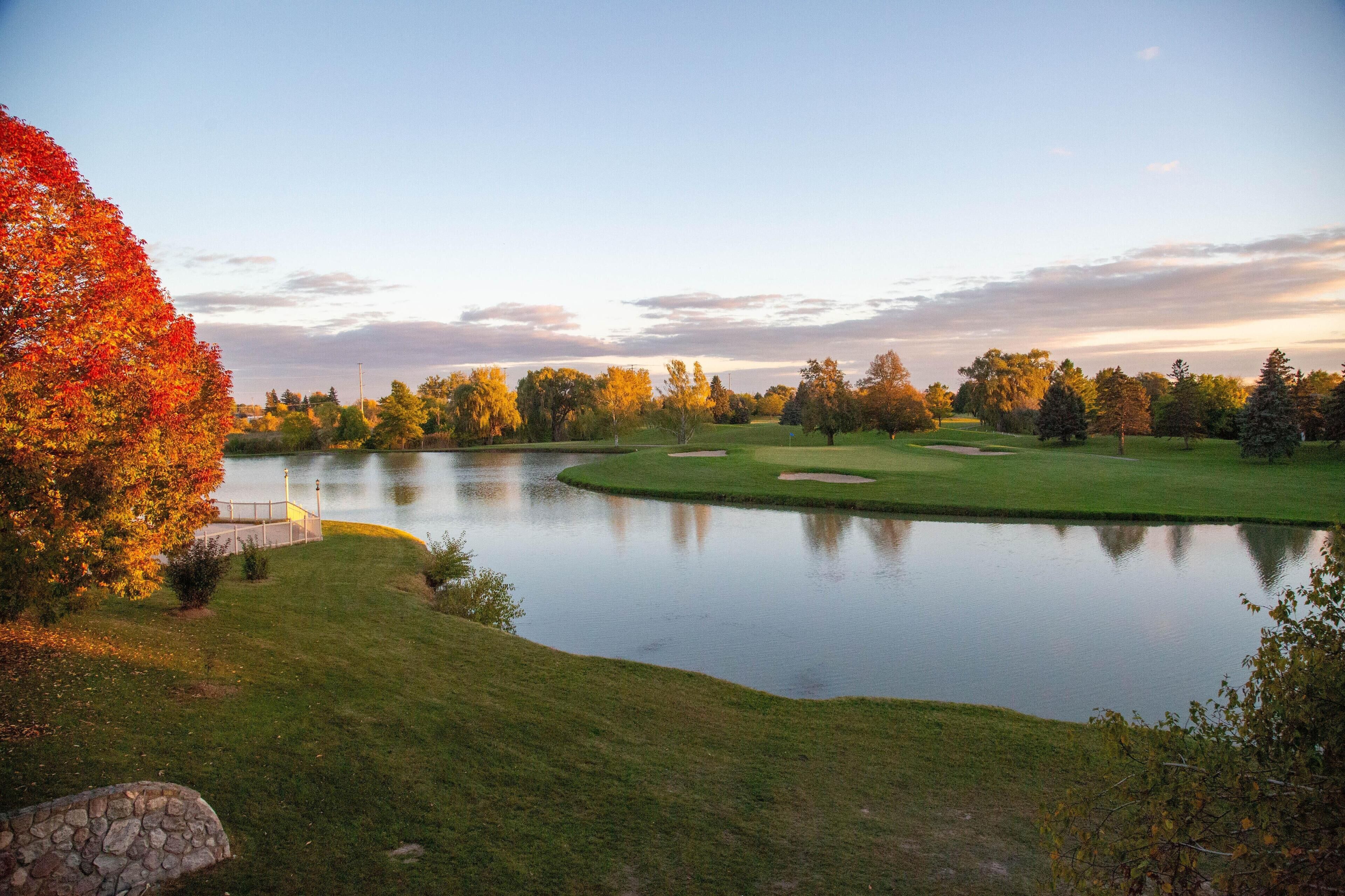 A serene golf course with a pond, surrounded by trees with autumn foliage.
